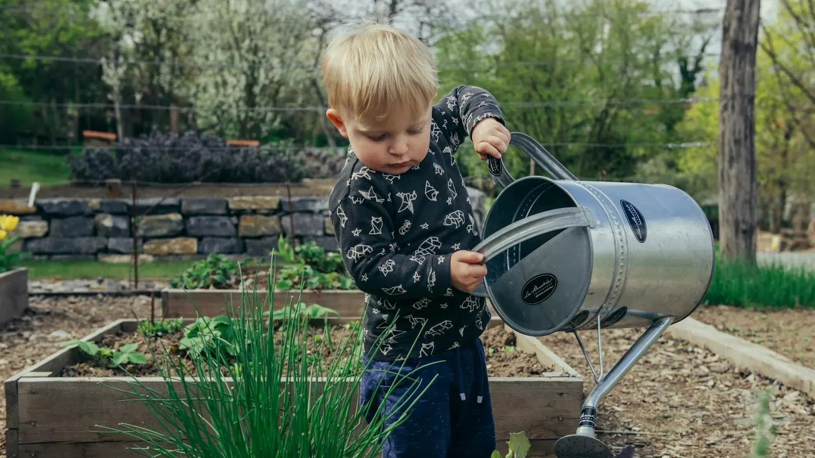 A young boy standing beside a watering can in a garden